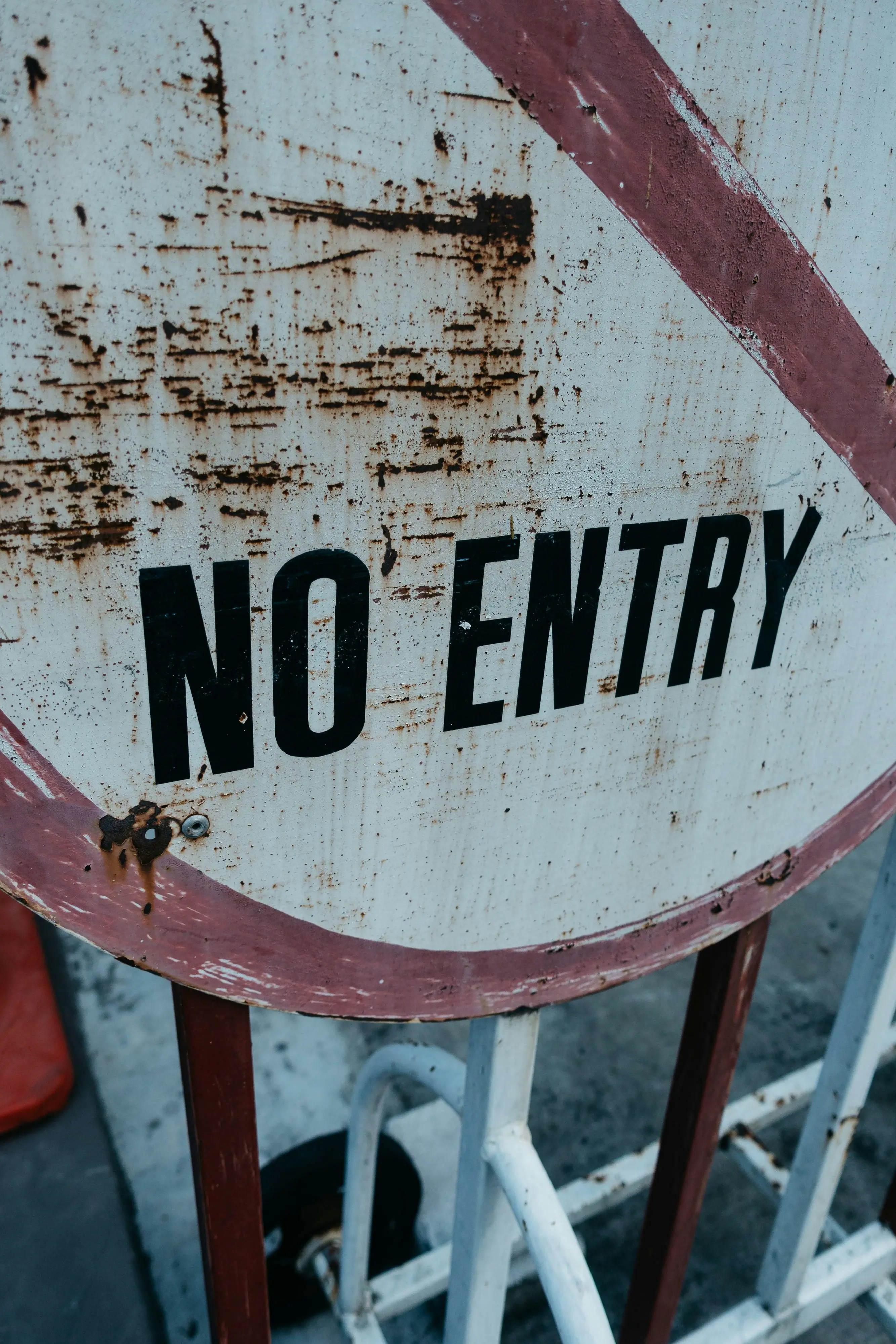 A close-up of a rusty and weathered 'No Entry' sign on a metal barricade